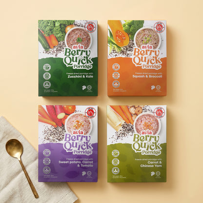 Four boxes of avia Berry Quick Porridge arranged in a 2x2 grid on a warm beige background, with a gold spoon and folded cream cloth in the lower left corner. The boxes feature different flavor color blocks: dark green (Zucchini & Kale), orange (Squash & Broccoli), purple (Sweet potato, Carrot & Tomato), and light green (Carrot & Chinese Yam).